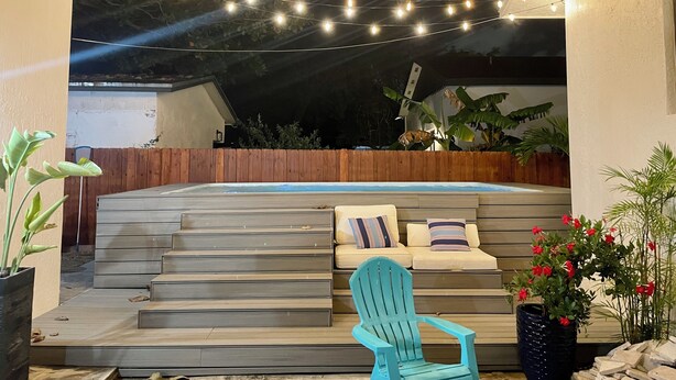 Un'area patio con gradini che conducono a una zona relax, luci decorative sospese e una vasca idromassaggio.