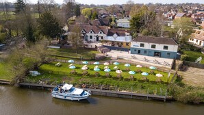 A riverside hotel with outdoor seating and a boat dock. - The Fleet (Tewkesbury)