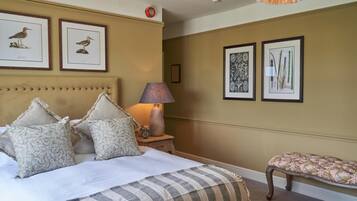 A bedroom with a large bed, a bedside table with a lamp, and framed botanical illustrations on the wall.