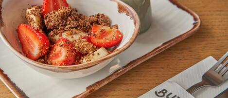 A bowl of granola with strawberries and yogurt on a ceramic plate, accompanied by a small cup and a napkin with text.