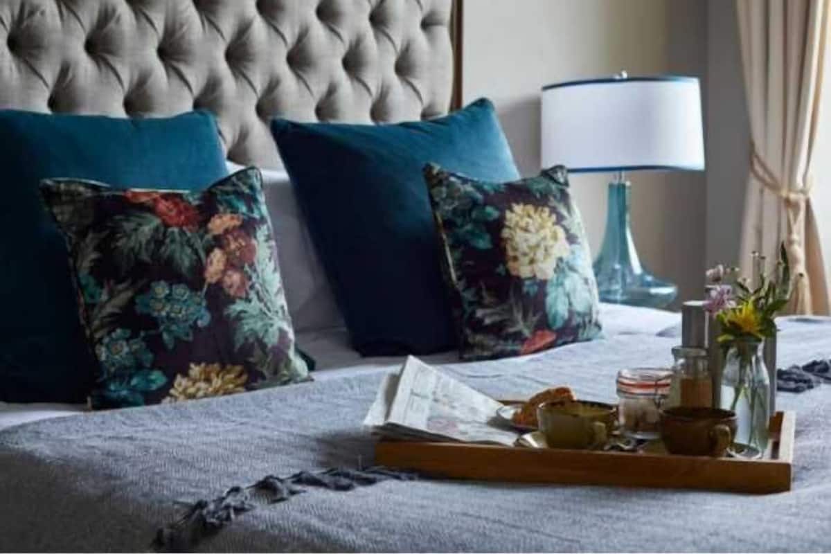 A neatly made bed with floral pillows, a bedside table with a lamp, and a tray with breakfast items.
