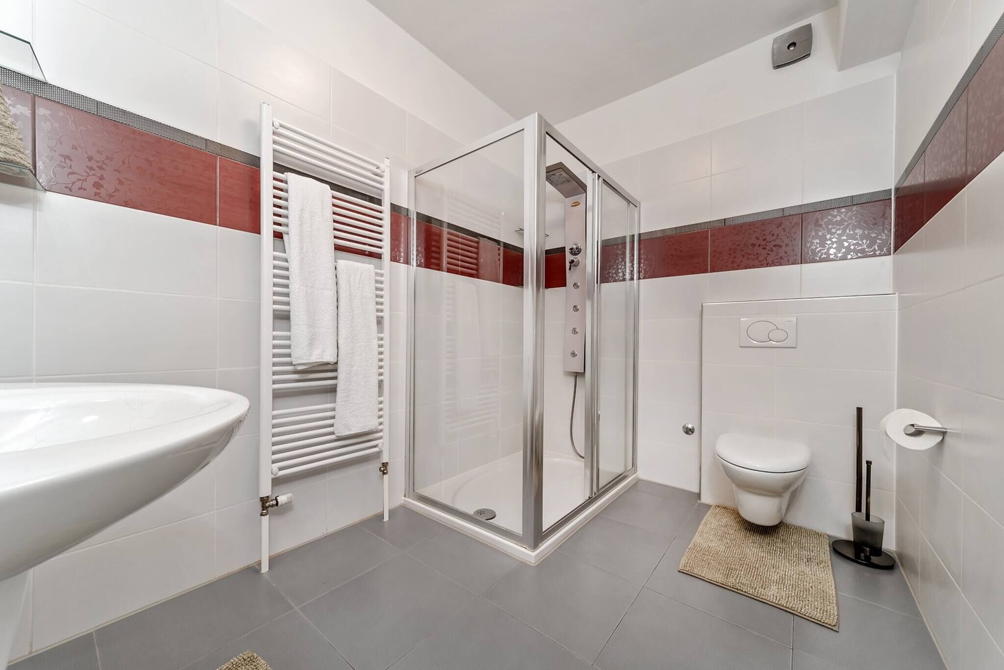 A bathroom with a white sink, a glass shower enclosure, a toilet, and a towel rack.
