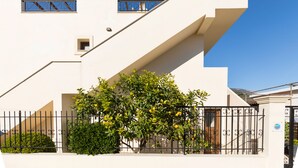 A modern building with a white facade, a black metal fence, and a tree with green leaves and yellow fruits. - Lemon Tree Corfu Apartments by Konnect (Corfu)