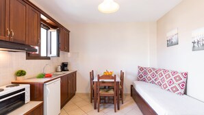 A compact kitchen with modern appliances, a dining area with a table and chairs, and a small bed with patterned pillows. - Lemon Tree Corfu Apartments by Konnect (Corfu)