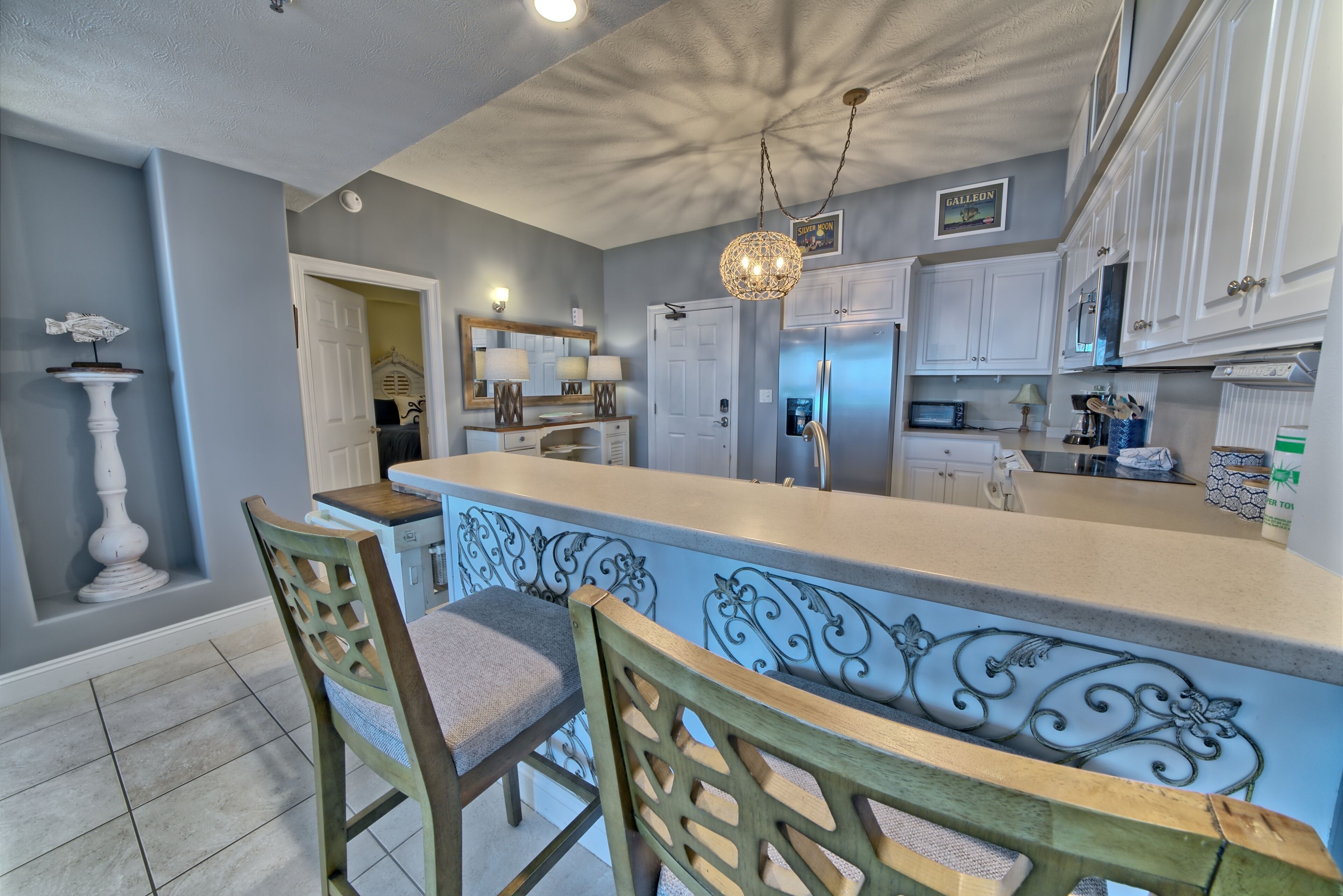 A kitchen with a central island, bar stools, white cabinets, and a chandelier.