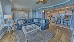 A living room with a sectional sofa, a glass coffee table, and a chandelier. - Cozy Oceanfront Condo with Beachside Pool - Unit 1602 by RedAwning (Panama City Beach)