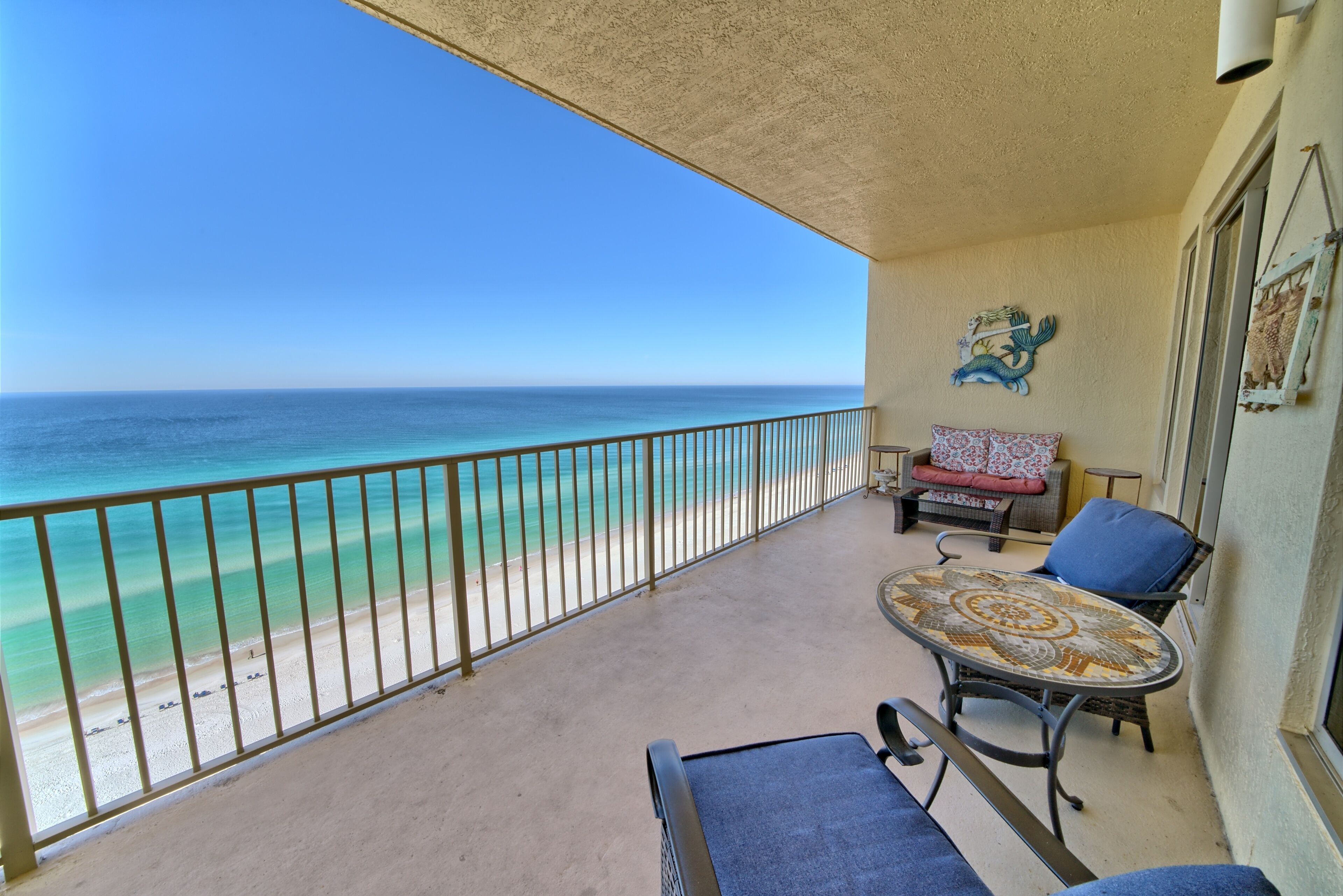A balcony with a view of the ocean, a table with a patterned tablecloth, and a chair.