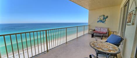 A balcony with a view of the ocean, a table with a patterned tablecloth, and a chair.
