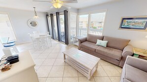 A spacious living room with a beige sofa, a coffee table, and a dining area with a white table and chairs. - SPC 2013 is a Pet Friendly Upstairs 1 BR with Seasonal Beach Setup by RedAwning (Destin)