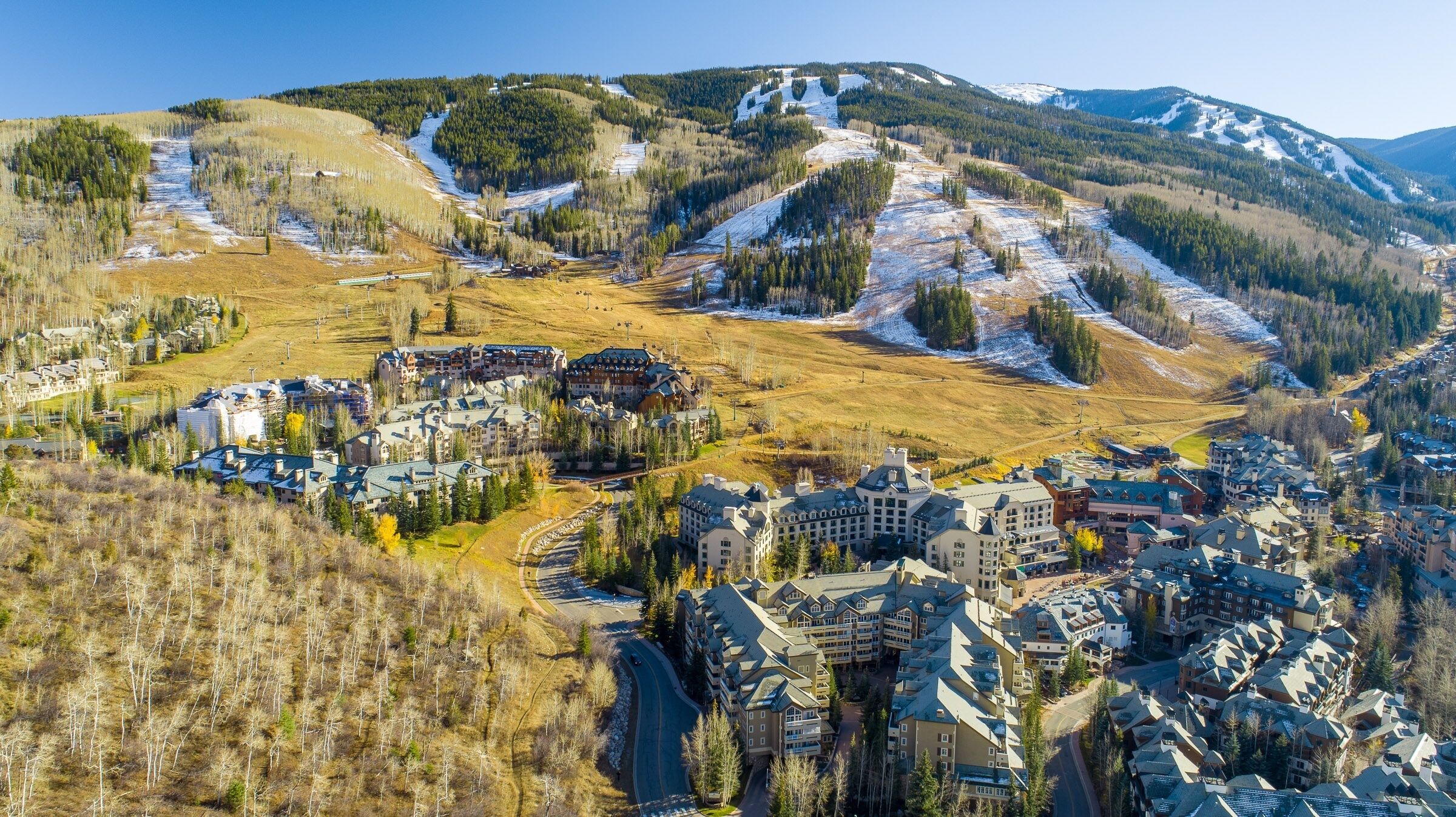 A mountainous resort town with multiple buildings, including hotels and lodges, surrounded by snow-covered slopes and dense forests.