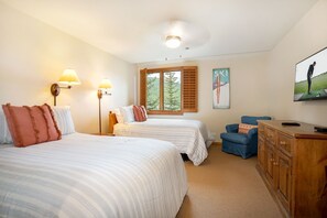 Een hotelkamer met twee bedden, een bureau, een stoel, een televisie en een raam met uitzicht op bomen.