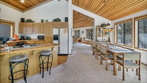 A spacious kitchen with wooden cabinets, a central island with stools, and large windows providing natural light. - 8 Crag Home with Private Indoor Hot Tub, Bike is Provided for Outdoor Activities by RedAwning (Bend)