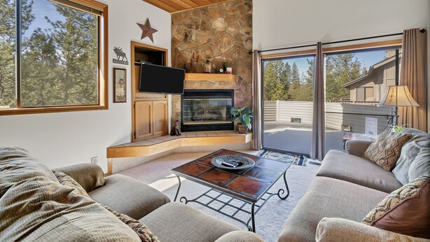 A cozy living room with a stone fireplace, comfortable seating, and large windows offering a view of the outdoors. - 8 Crag Home with Private Indoor Hot Tub, Bike is Provided for Outdoor Activities by RedAwning (Bend)