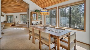 A spacious dining area with a wooden table and chairs, large windows with a forest view, and a ceiling with wooden slats. - 8 Crag Home with Private Indoor Hot Tub, Bike is Provided for Outdoor Activities by RedAwning (Bend)
