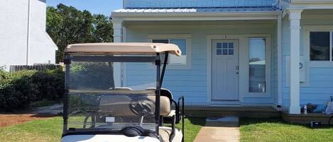Un carrito de golf estacionado en la entrada de una casa de dos pisos con fachada azul claro y techo color beige.