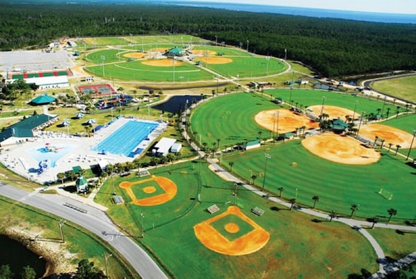 Luchtbeeld van een sportcomplex met meerdere honkbalvelden, een zwembad en tennisbanen.