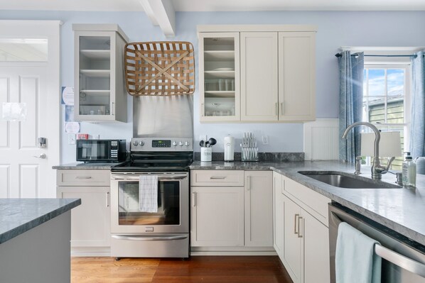A modern kitchen with white cabinets, stainless steel appliances, and a large window with curtains. - The Blackberry Suite | 3 BR 2BA | 2nd Floor Condo (Charleston)