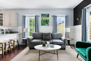 A modern living room with a grey sofa, a green armchair, a round coffee table, and a painting of a green landscape on the wall. - The Blackberry Suite | 3 BR 2BA | 2nd Floor Condo (Charleston)