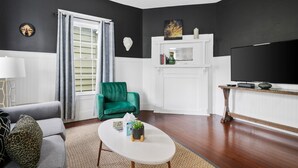 A living room with a dark wall, a green armchair, a white coffee table, and a flat-screen TV. - The Blackberry Suite | 3 BR 2BA | 2nd Floor Condo (Charleston)