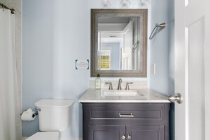 A bathroom with a white toilet, a dark vanity with a sink, and a mirror above the vanity. - The Blackberry Suite | 3 BR 2BA | 2nd Floor Condo (Charleston)