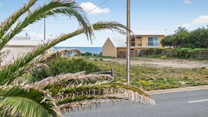 Una propiedad costera con una casa, una zona arenosa con flores amarillas y una palmera en primer plano.