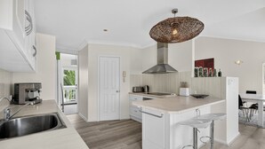 Una cocina moderna con una isla central, horno empotrado, cafetera y lámpara colgante.