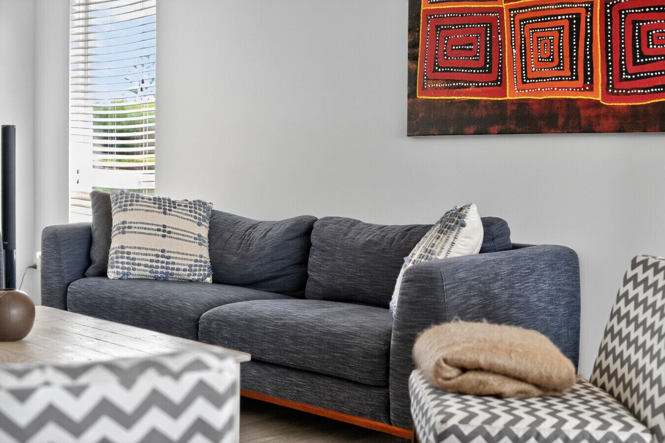 A modern living room with a grey sofa, patterned pillows, a small table, and a decorative wall piece.