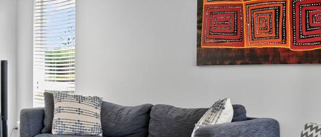 A modern living room with a grey sofa, patterned pillows, a small table, and a decorative wall piece.