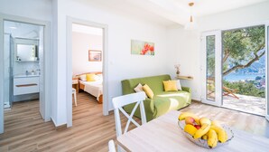 A bright room with a wooden floor, a green sofa, a white chair, and a table with a fruit bowl. - Away from everyone, close to everything (Dubrovnik)