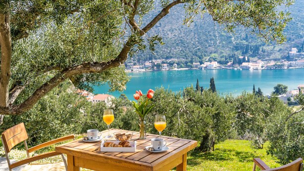 A wooden table with breakfast items and drinks, overlooking a lake and town. - Away from everyone, close to everything (Dubrovnik)