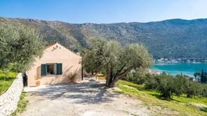 A rustic building with a dirt path leading to a wooden table and chairs, surrounded by olive trees and a view of a lake and mountains. - Away from everyone, close to everything (Dubrovnik)