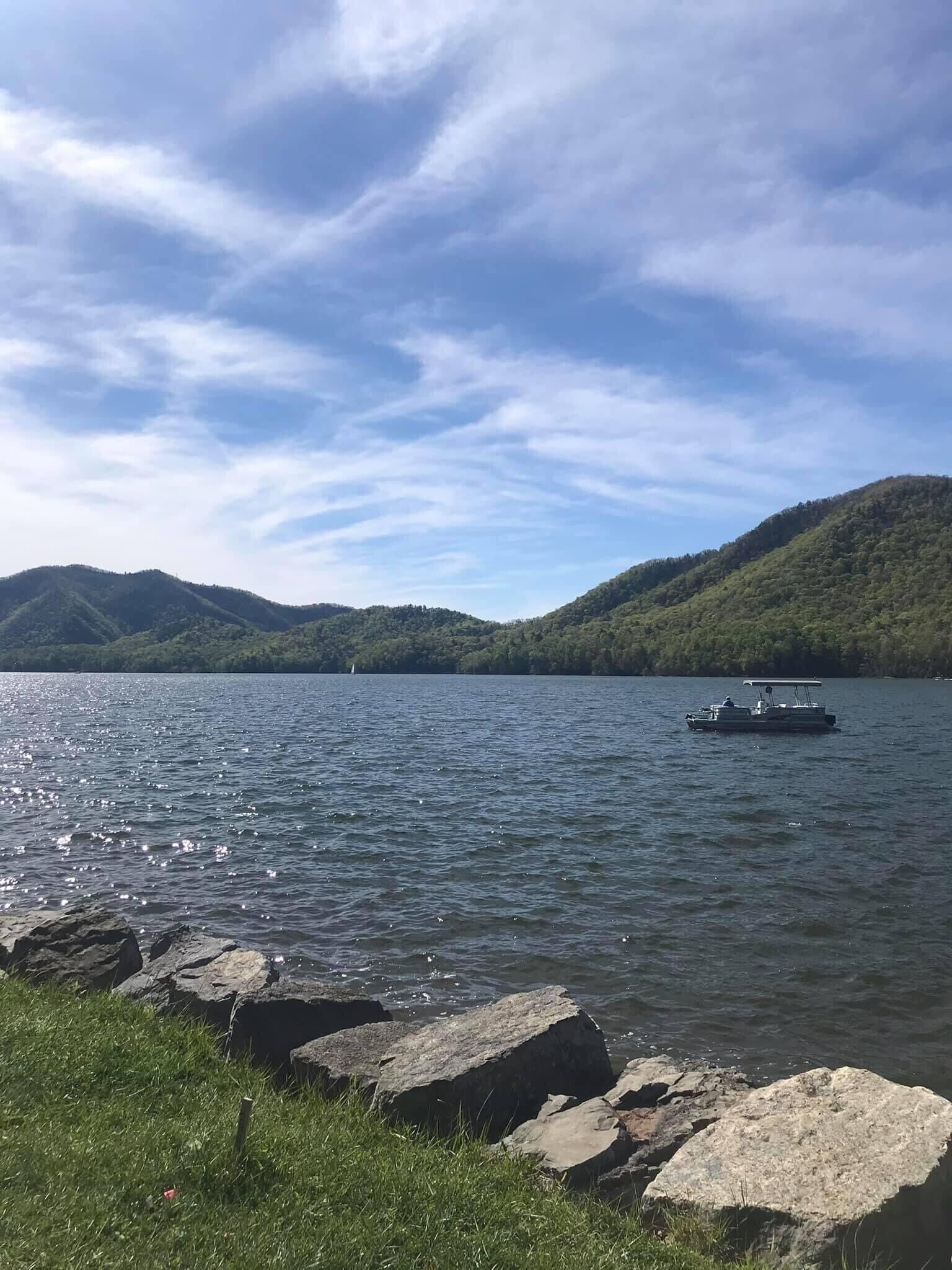 Un llac amb una barca, envoltat de turons i un cel serè.