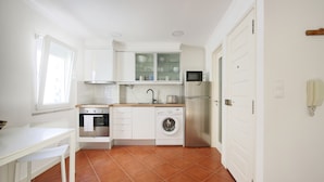 A compact kitchen with white cabinetry, a built-in oven, a washing machine, and a microwave. - 3 guest apartment in the center of Alfama (Lisboa)