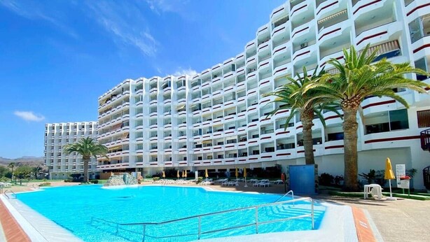 A large swimming pool with a tiled deck, surrounded by palm trees and a multi-story hotel building with balconies. - Agaete Park 128 By Pride Holiday Rentals (Playa del Ingles)