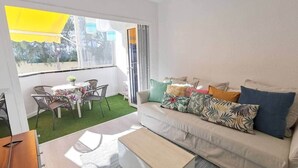 A modern living room with a sofa, coffee table, and a dining area with chairs and a table. - Agaete Park 128 By Pride Holiday Rentals (Playa del Ingles)
