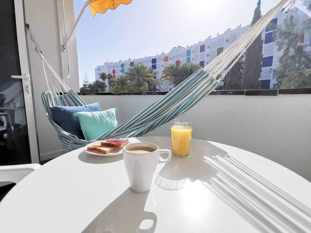 Un balcón con una hamaca, una mesa con artículos para el desayuno y vistas a edificios.