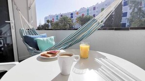 A balcony with a hammock, a table with breakfast items, and a view of buildings. - Agaete Park 128 By Pride Holiday Rentals (Playa del Ingles)