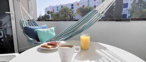 Un balcón con una hamaca, una mesa con artículos para el desayuno y vistas a edificios.