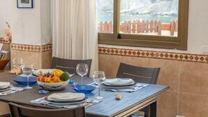 Une table à manger dressée avec des assiettes, des bols et des verres, offrant une vue sur la mer par une fenêtre.
