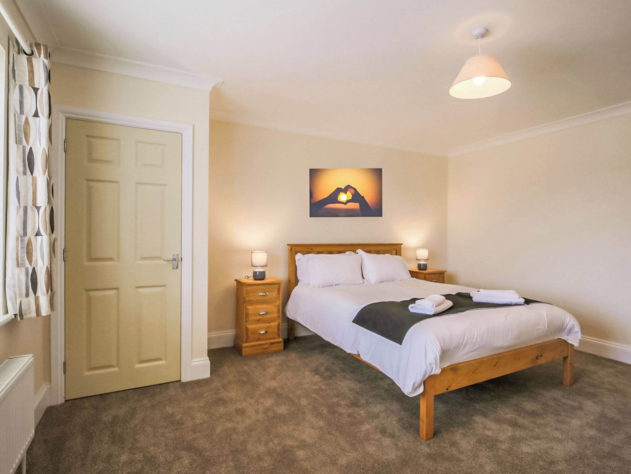 A bedroom with a bed, two bedside tables, a nightstand, a door, and a wall-mounted picture.