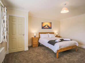 A bedroom with a bed, two bedside tables, a nightstand, a door, and a wall-mounted picture.