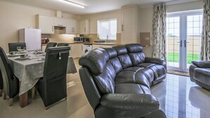 A modern living room with a leather sofa, dining area with chairs, a kitchen with appliances, and a sliding glass door to a patio.