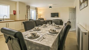 A dining area with a table set for six, a television mounted on the wall, and a window with curtains.
