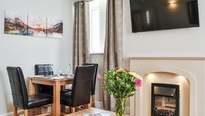 En matplats med ett träbord, svarta läderstolar, en vas med blommor och en platt-TV som är monterad på väggen.