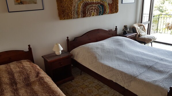 Un dormitorio con una cama de madera, una mesita de noche con lámpara, una silla y una ventana con vistas al verdor.