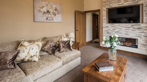 A living room with a sectional sofa, a wooden coffee table, a fireplace, and a TV mounted on the wall. - Sycamore Barn - UK33353 (Northowram, near Halifax)