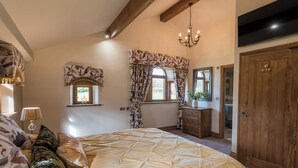 A bedroom with a large bed, a chandelier, a wooden wardrobe, and a window with curtains. - Sycamore Barn - UK33353 (Northowram, near Halifax)