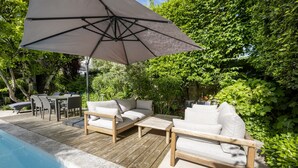 Una terraza de madera con mobiliario exterior, piscina y abundante vegetación.