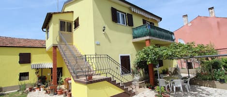 A yellow building with a staircase, outdoor seating, and potted plants.