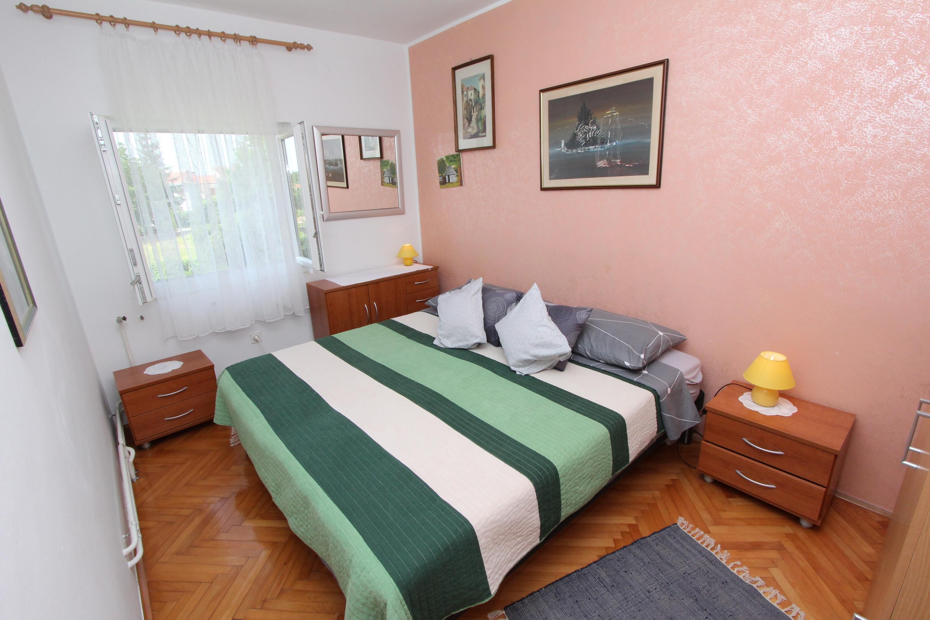 Une chambre à coucher avec un lit, des tables de chevet en bois, une table de chevet avec une lampe, une fenêtre avec des rideaux et des œuvres d’art murales.